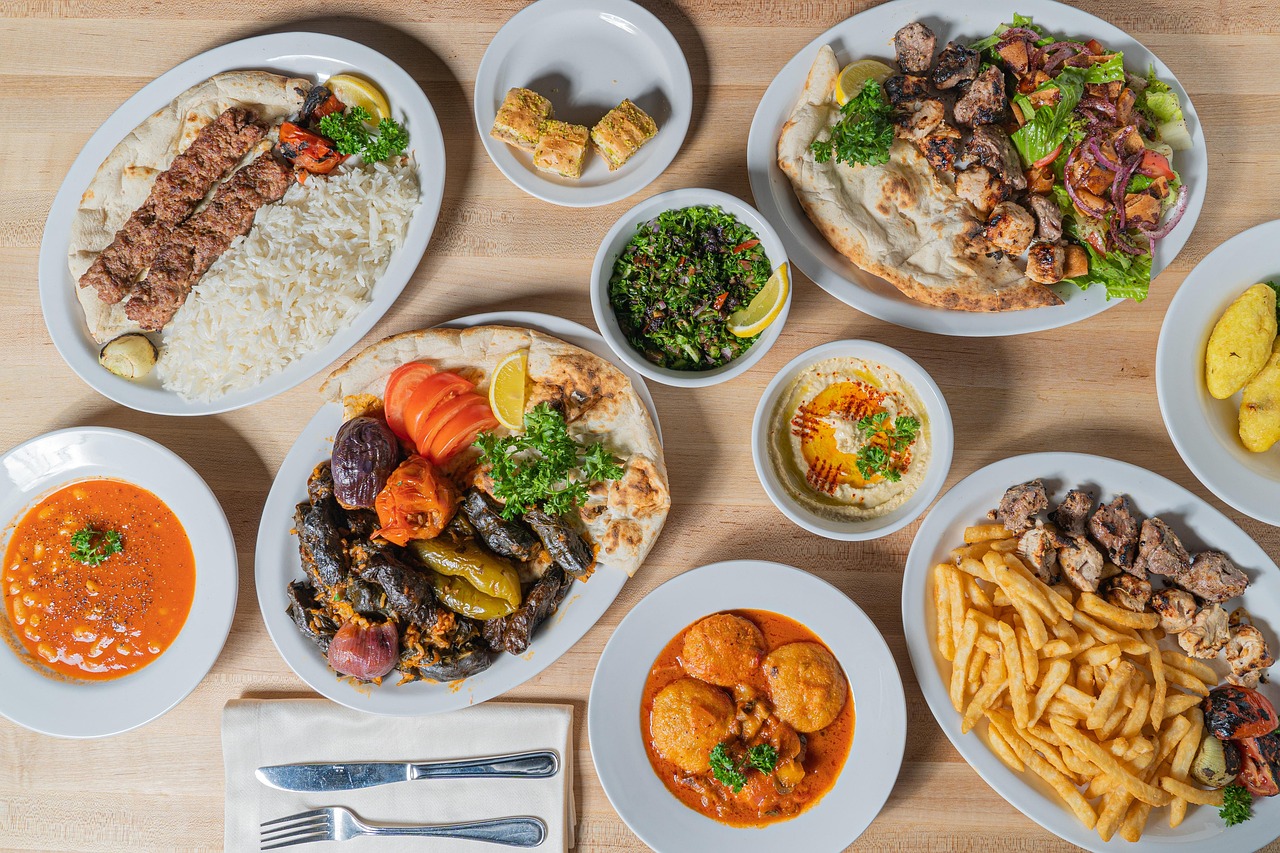 A table spread with Mediterranean plates: kebab over rice, stuffed vegetables, hummus, tabbouleh and baklava